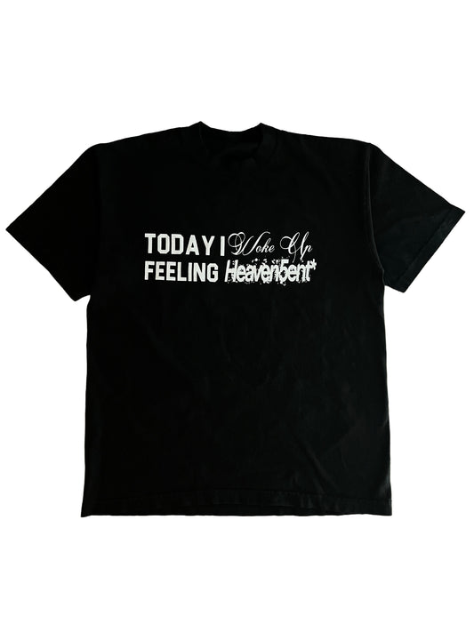 A black short-sleeve t-shirt with white graphic text on the front reading 'TODAY I Wake Up FEELING Heaven Sent' on a plain white background.